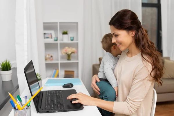 Madre feliz con el bebé y el ordenador portátil trabajando en casa —  Fotos de Stock