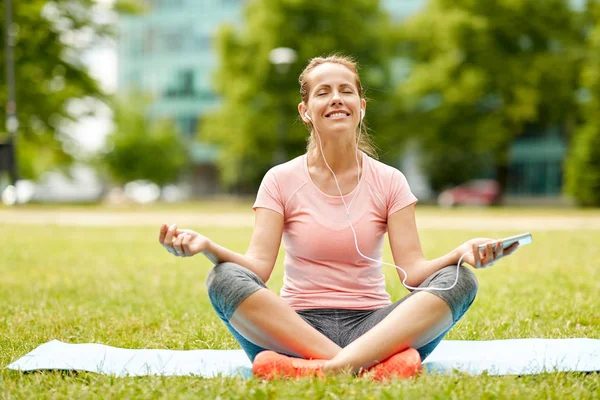 Vrouw met smartphone en hones mediteren op park — Stockfoto