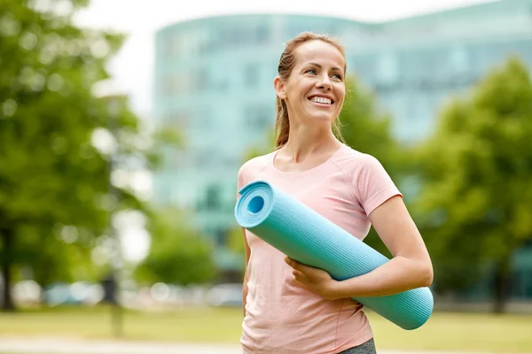 Lyckligt leende kvinna med träningsmatta på city park — Stockfoto