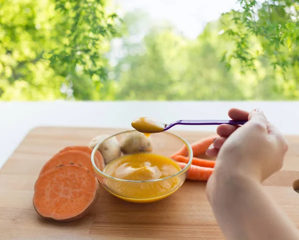 Hand med vegetabiliska puré eller barnmat i sked — Stockfoto