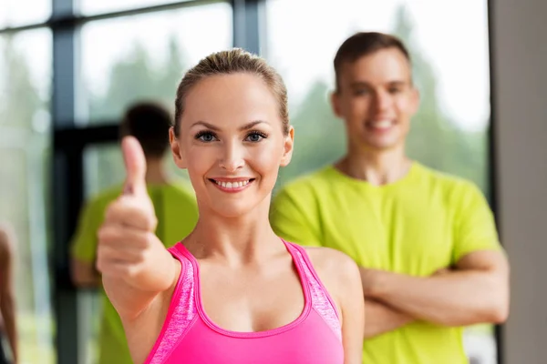 Sonriente hombre y mujer mostrando pulgares hacia arriba en el gimnasio —  Fotos de Stock