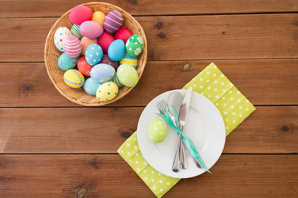 Húsvéti tojás kosárban, tányérokban, evőeszközökben és virágokban — Stock Fotó