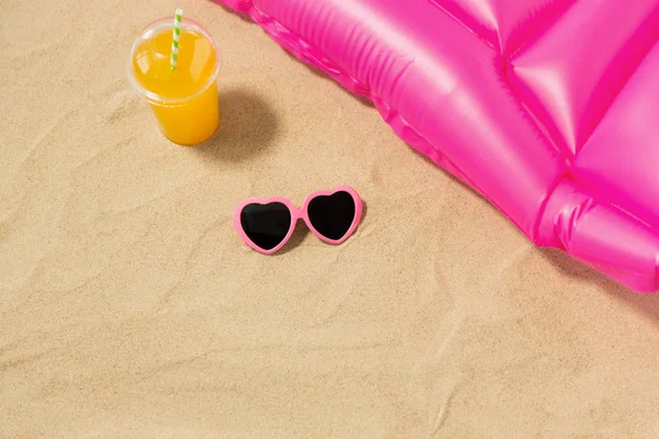 Lunettes de soleil, jus et matelas de piscine sur sable de plage — Photo