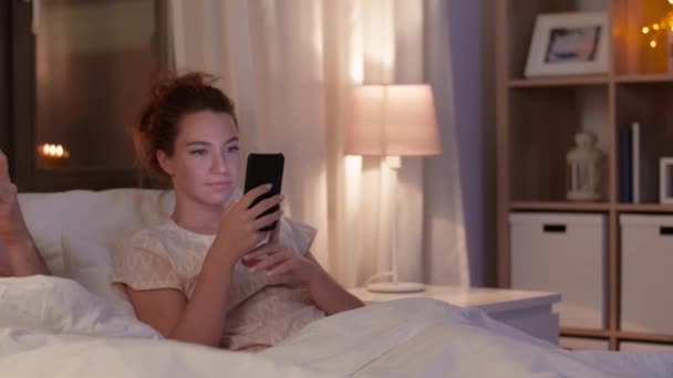 Pareja usando teléfonos inteligentes en la cama por la noche — Vídeo de stock