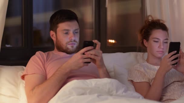 Par som använder smartphones i sängen på natten — Stockvideo