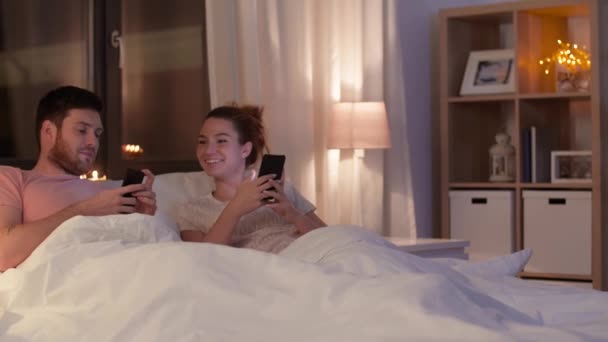 Glückliches Paar nutzt Smartphone nachts im Bett — Stockvideo