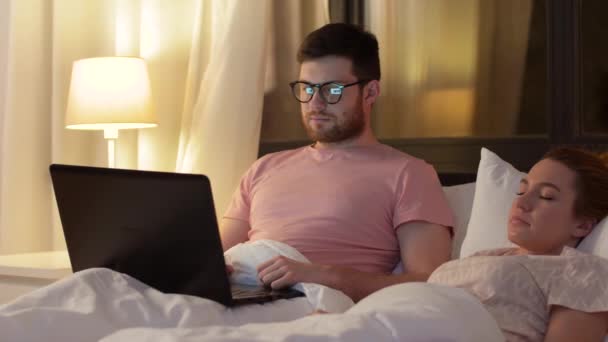 Мужчина использует ноутбук, пока подруга спит — стоковое видео