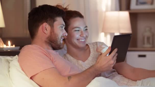 Ευτυχισμένο ζευγάρι χρησιμοποιώντας υπολογιστή tablet στο κρεβάτι τη νύχτα — Αρχείο Βίντεο