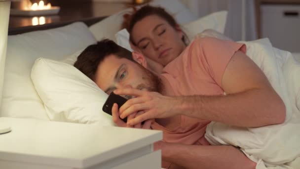 Hombre usando el teléfono inteligente mientras su novia está durmiendo — Vídeos de Stock