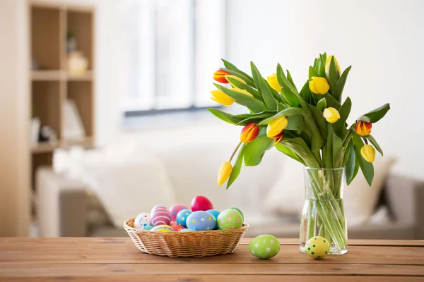 Colored easter eggs in basket and flowers at home — Stock Photo, Image