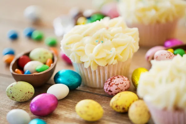 Magdalenas con huevos de chocolate y caramelos en la mesa — Foto de Stock