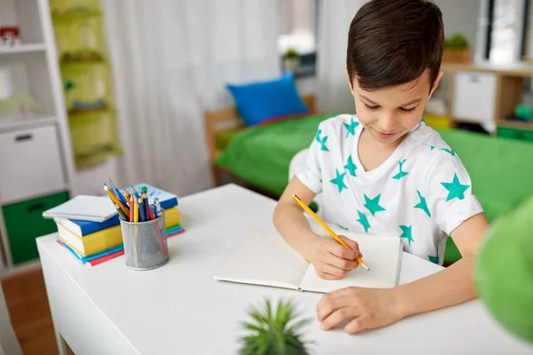 Niño feliz escribiendo o dibujando a la libreta en casa —  Fotos de Stock