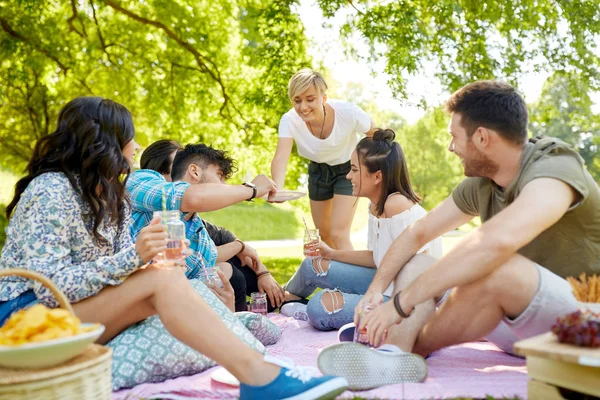 Amici con bevande e cibo al picnic nel parco — Foto Stock