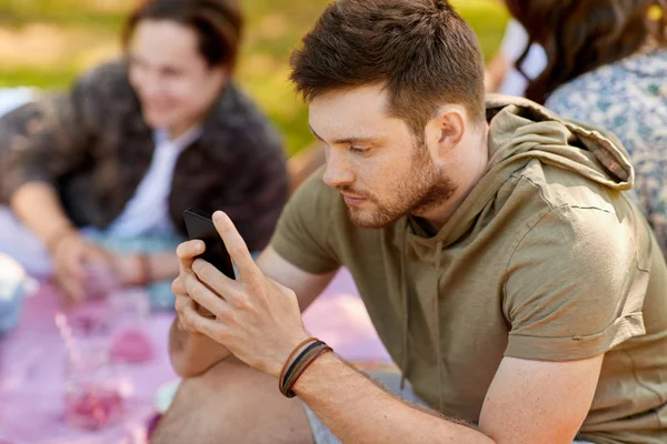 Man met smartphone op picnic met vrienden — Stockfoto