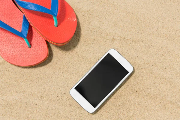 Smartphone e infradito sulla sabbia della spiaggia — Foto Stock