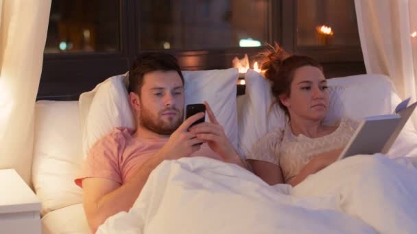 Paar mit Smartphone und Buch nachts im Bett — Stockvideo