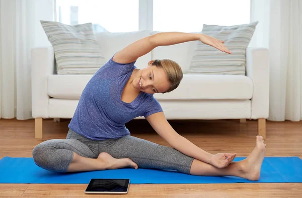 Woman with tablet computer doing yoga at home — Stock Photo, Image