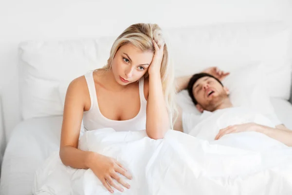 Unhappy woman in bed with snoring sleeping man — Stock Photo, Image