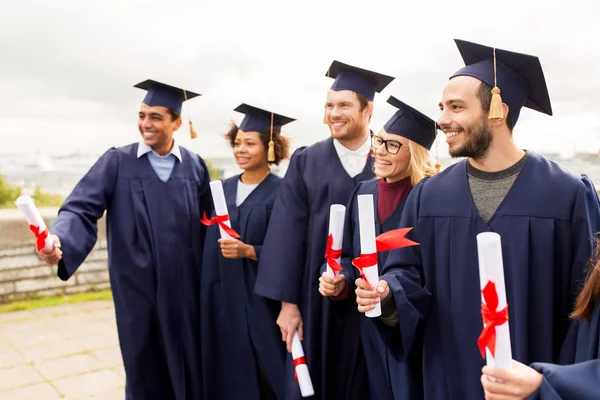 Estudantes felizes em placas de argamassa com diplomas — Fotografia de Stock