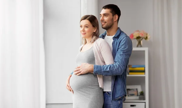 Uomo abbracciare donna incinta alla finestra a casa — Foto Stock