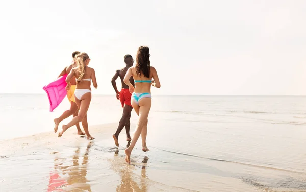 Freunde laufen mit Beachball und Badematratze — Stockfoto