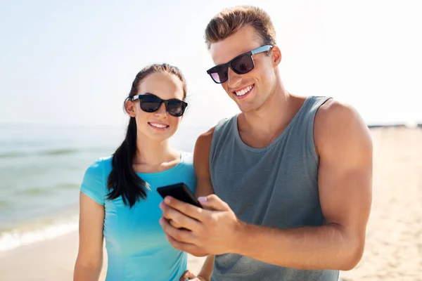 Couple in sports clothes with smartphones on beach — Stock Photo, Image