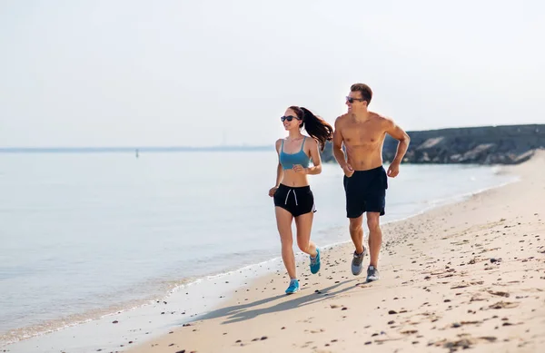 Koppel in sport kleding lopen langs op het strand — Stockfoto