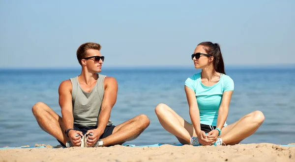 Sorrindo casal alongamento pernas na praia — Fotografia de Stock