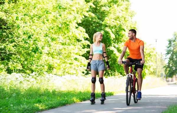 Happy couple with rollerblades and bicycle riding — Stock Photo, Image