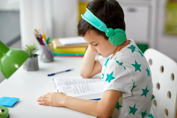 Jongen in hoofdtelefoon met leerboek thuis leren — Stockfoto