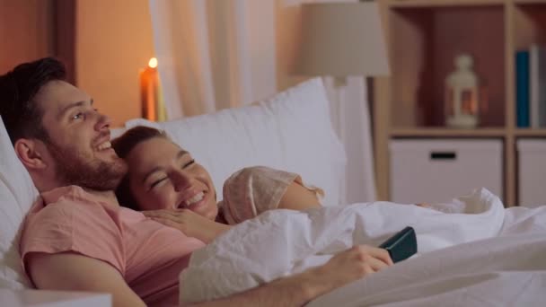 Feliz pareja viendo la televisión en la cama por la noche en casa — Vídeos de Stock