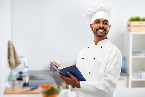 Щасливий чоловічий індійський шеф-кухар з кулінарною книгою на кухні — стокове фото
