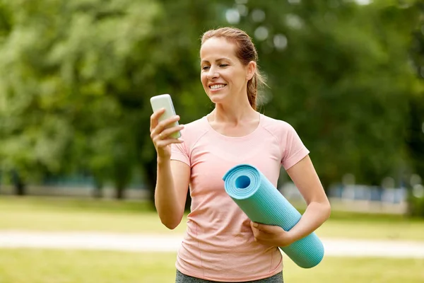 Γυναίκα με χαλί άσκησης και smartphone στο πάρκο — Φωτογραφία Αρχείου