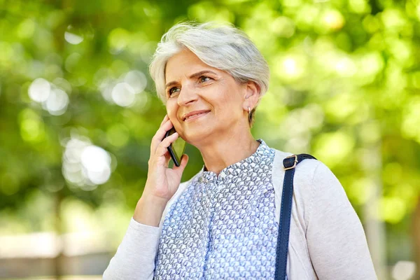 Старша жінка телефонує на смартфон в літньому парку — стокове фото