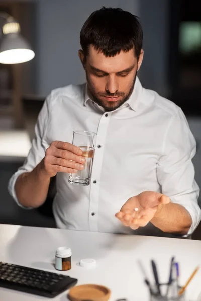 Zakenman met geneeskunde pillen bij nacht kantoor — Stockfoto