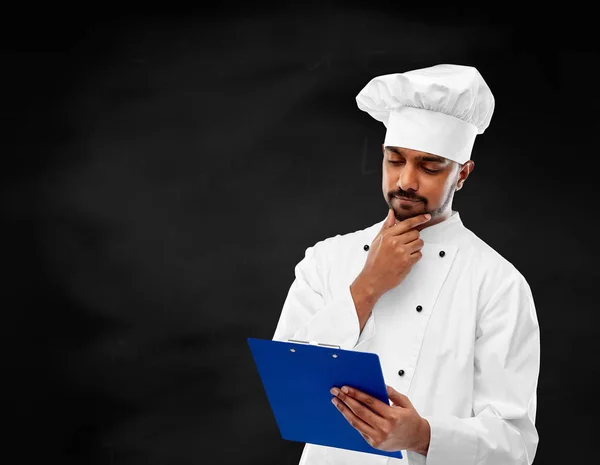 Koch liest Menü auf Klemmbrett über Tafel — Stockfoto