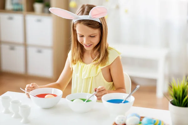 Meisje kleuren paaseieren door vloeibare kleurstof thuis — Stockfoto