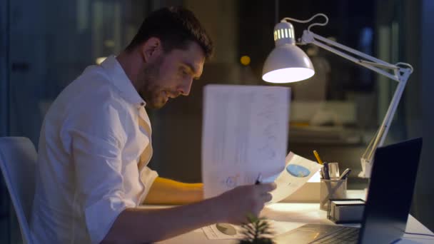 Бизнесмен с бумагами и ноутбуком в ночном офисе — стоковое видео