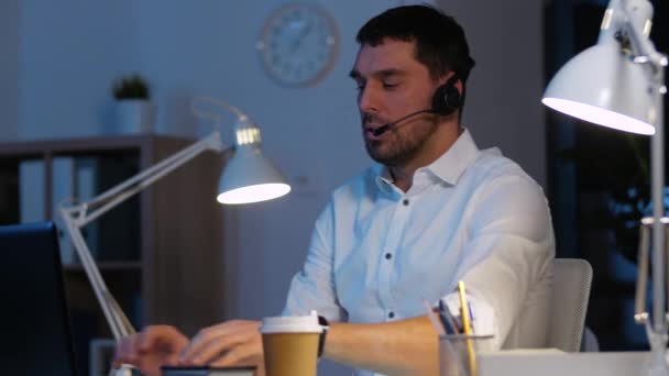 Homem de negócios em fone de ouvido com laptop no escritório da noite — Vídeo de Stock