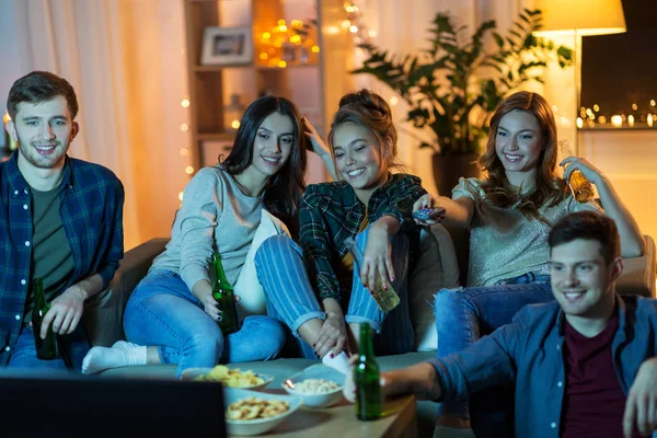 Amigos com bebidas e lanches assistindo tv em casa — Fotografia de Stock