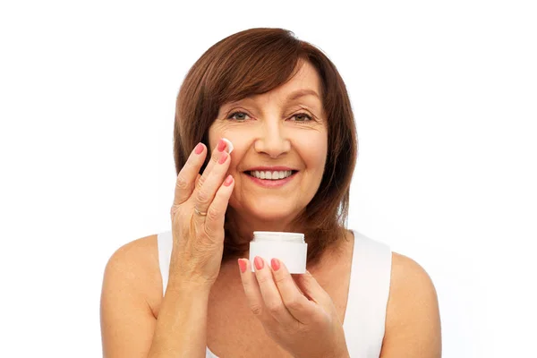 Sorridente donna anziana applicando crema al suo viso — Foto Stock