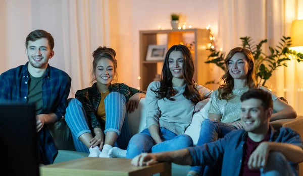 Amigos felices viendo la televisión en casa por la noche — Foto de Stock