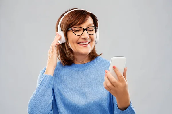 Femme âgée dans les écouteurs écouter de la musique sur cellulaire — Photo