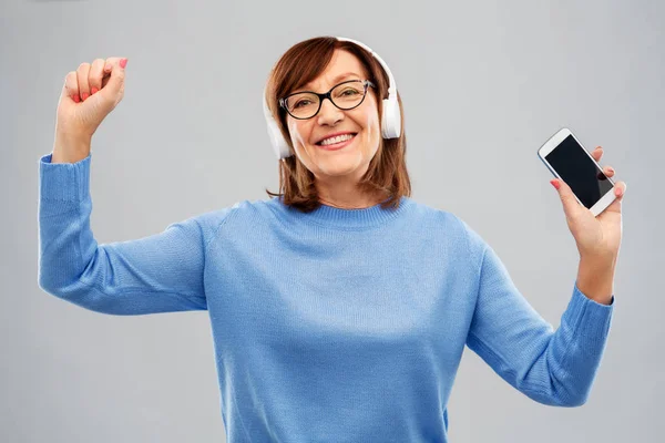 Femme âgée dans les écouteurs écouter de la musique sur cellulaire — Photo