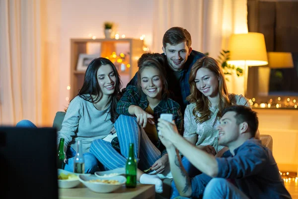 Amici con smartphone guardando la tv a casa — Foto Stock