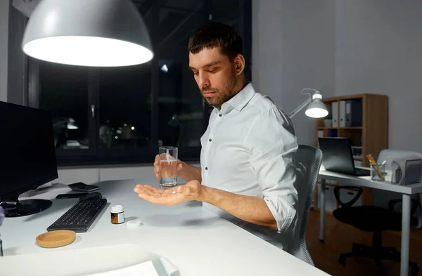 Businessman taking medicine pill at night office — Stock Photo, Image