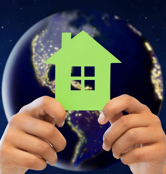 Hands holding green house over earth in space Royalty Free Stock Photos