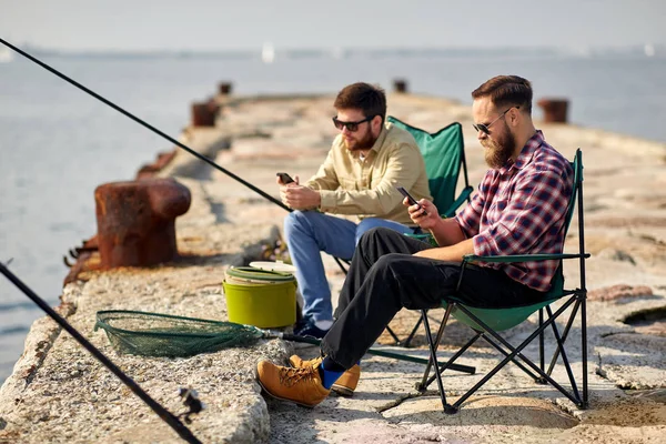 Amigos com smartphones pescando no cais no mar — Fotografia de Stock