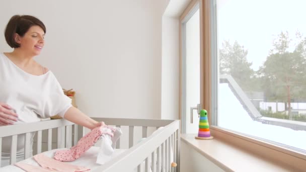 Szczęśliwy w ciąży kobieta ustawienie ubrania dla dzieci w domu — Wideo stockowe