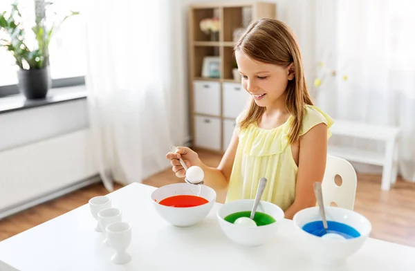 Девушка раскрашивает пасхальные яйца жидким красителем дома — стоковое фото